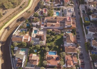An aerial view of homes and swimming pools beside a dried riverbed.