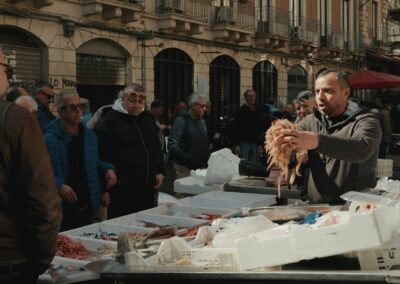 A fishmonger holding shrimp at a busy Mediterranean street market.